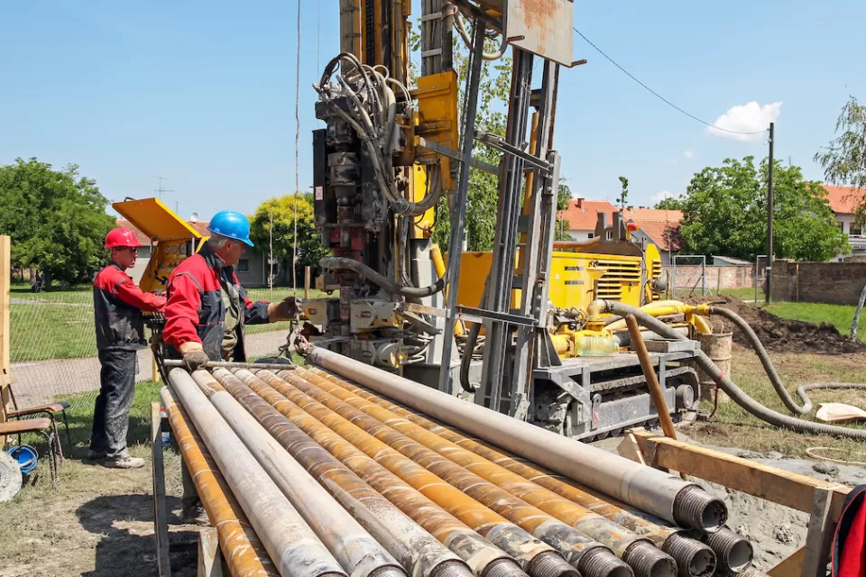 Workers next to excavator digging a geothermal well.